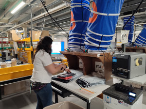 Les robots viennent faciliter le travail des équipes. Ici, l’opératrice s’occupe d’emballer plusieurs articles d’une même commande déposés par les robots via le toboggan bleu. - © Républik Retail